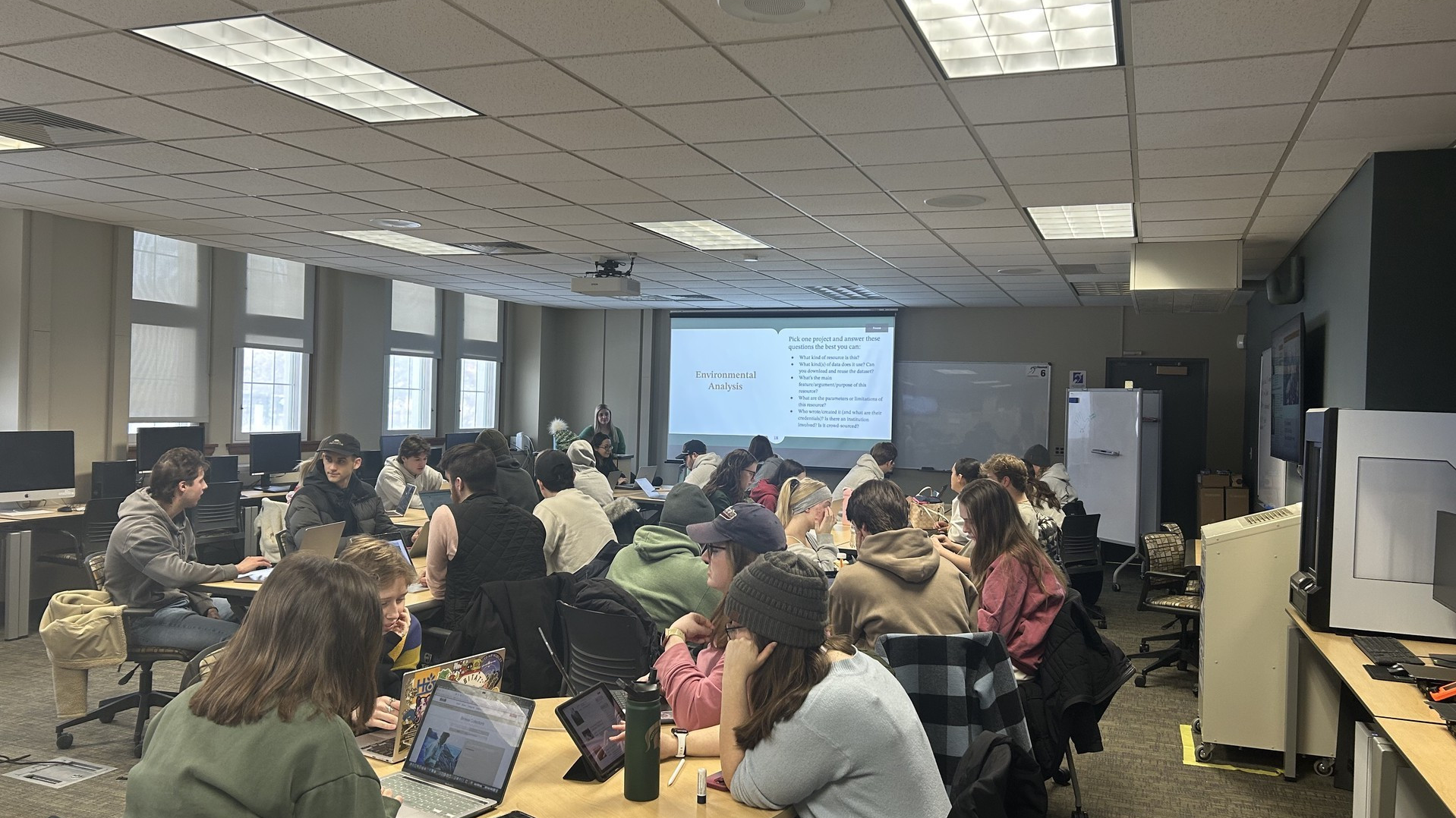 students at tables in a lab, with large screen showing powerpoint for workshop