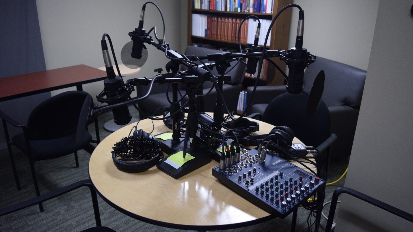 four microphones, a soundboard, audio mixer and headphones for podcsting on a table within the AV studio